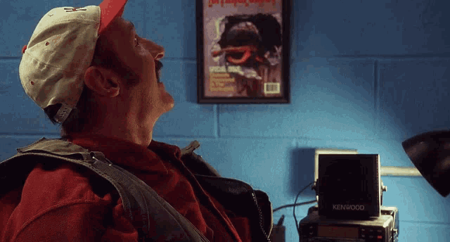 a man sitting in front of a kenwood radio with a magazine on the wall behind him