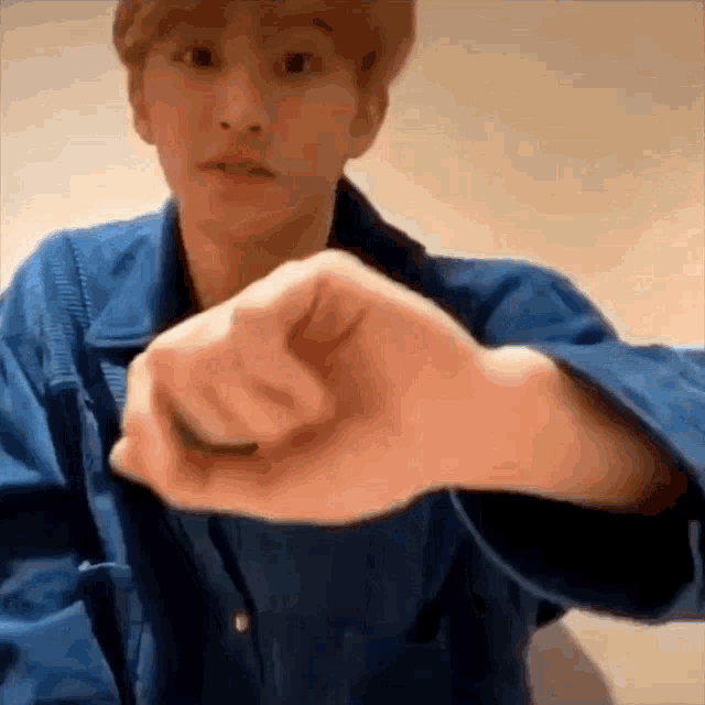 a man wearing a blue jacket is making a heart shape with his hands .