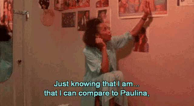 a woman is sitting in a room with posters on the wall and says just knowing that i am