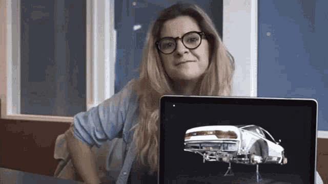 a woman wearing glasses is holding a laptop with a picture of a car on it