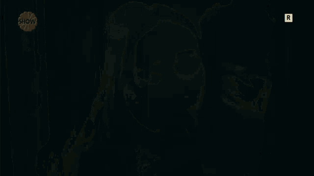a woman stands in a dark room with a show logo behind her