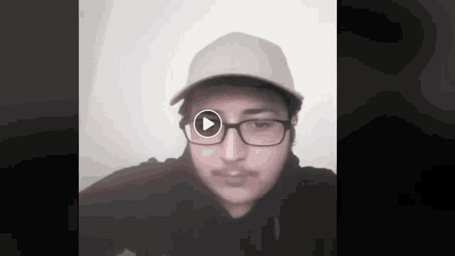 a man wearing glasses and a hat looks at the camera