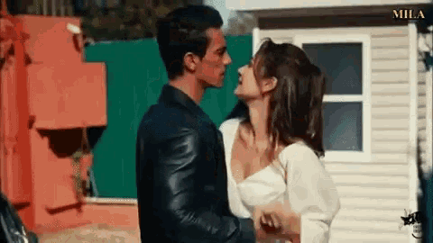 a man and a woman are kissing each other in front of a building .