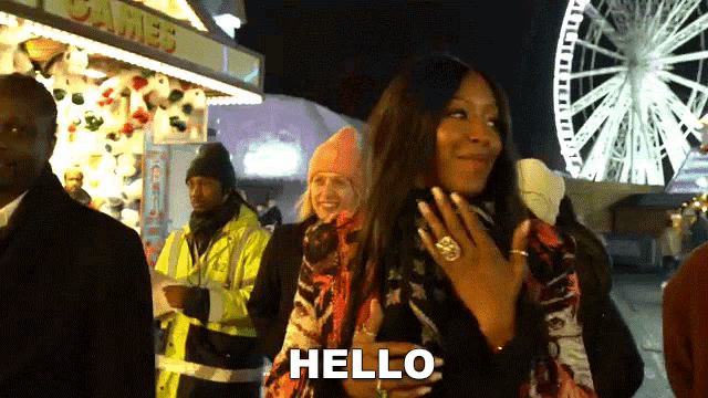 a woman stands in front of a ferris wheel and says " hello "