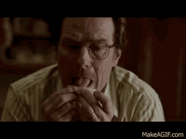 a man with glasses is eating a sandwich with his tongue out .