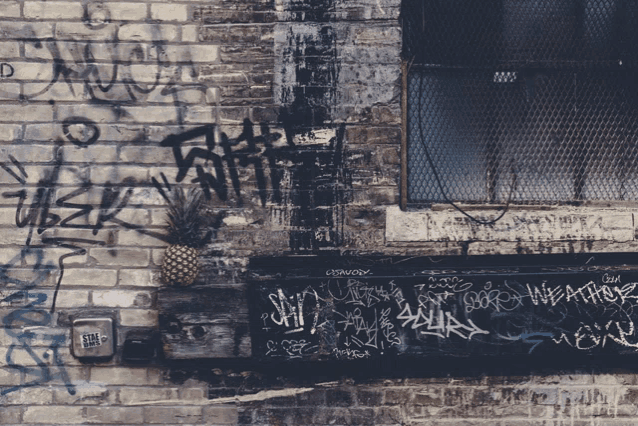 a pineapple is hanging on a brick wall with graffiti on it including one that says chronic
