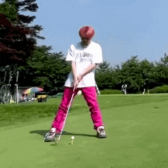 a man in a white shirt and pink pants is swinging a golf club on a green field .