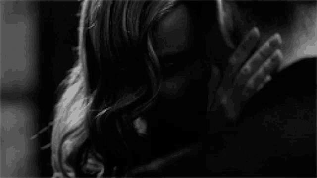 a black and white photo of a woman kissing a man on the neck .