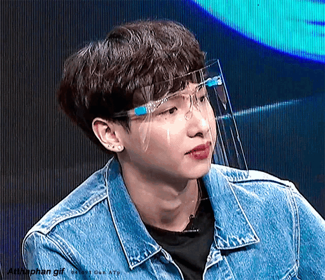 a young man wearing a denim jacket and a face shield is sitting on a stage .