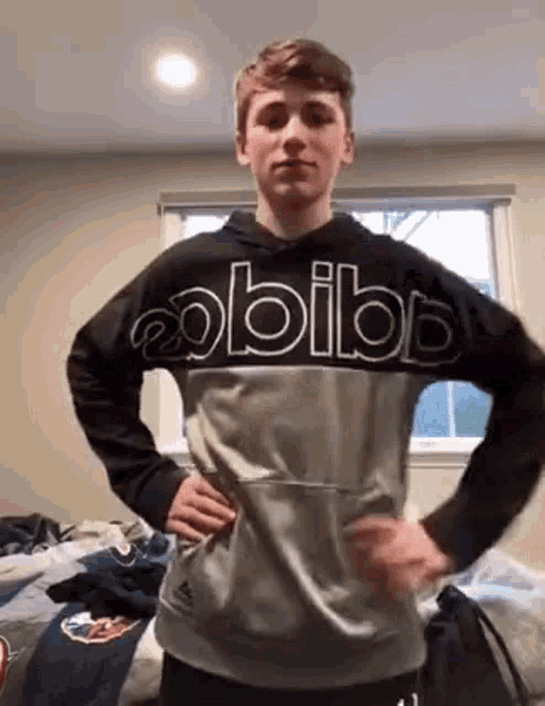 a young man is standing in a room with his hands on his hips wearing a hoodie .
