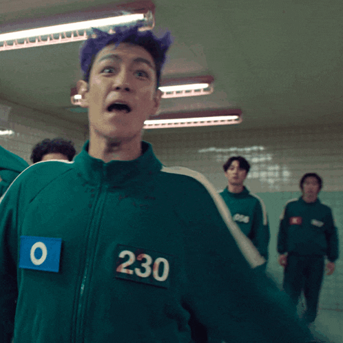 a man with purple hair wears a green jacket with the number 230 on it
