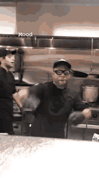 a man in a chef 's uniform is dancing in a kitchen while another man looks on .