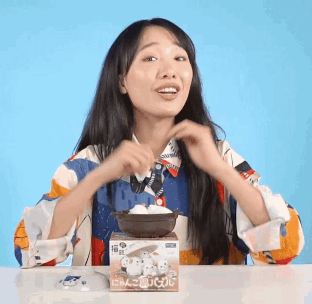 a woman sitting at a table with a box that says ' puzzle ' on it next to a bowl of food