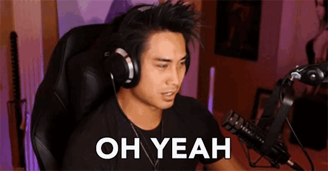 a man wearing headphones and a black shirt is sitting in front of a microphone and says oh yeah .