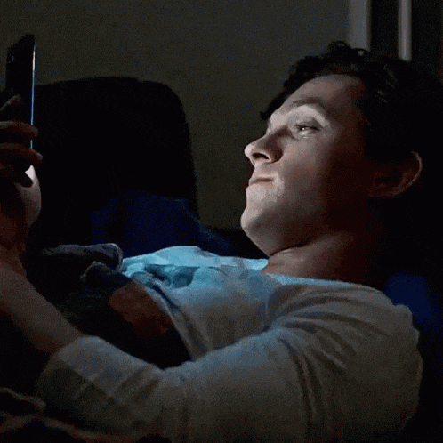 a woman is laying on a bed looking at her phone and making a funny face .