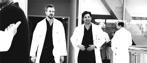 a black and white photo of two doctors standing next to each other in a hospital hallway .