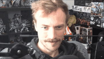 a man with a mustache looks at the camera in front of a sign that says ' a '