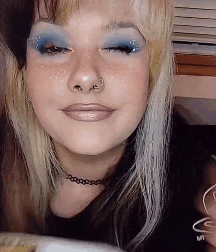 a close up of a woman 's face with blue eyeshadow and a nose ring