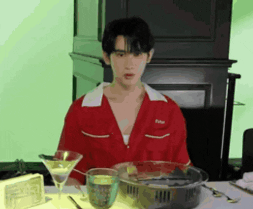 a young man in a red shirt is sitting at a table with a martini glass and a bowl of food .