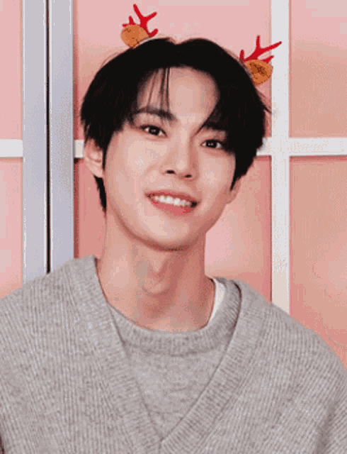 a young man wearing a sweater and reindeer antlers on his head is waving .