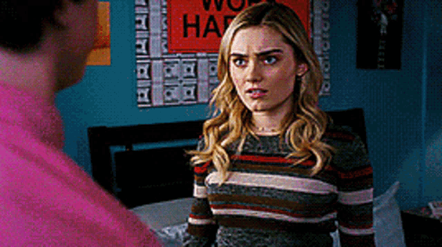 a woman in a striped sweater stands next to a man in a pink shirt in a bedroom .