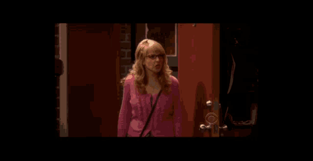 a woman in a pink sweater stands in front of a red door
