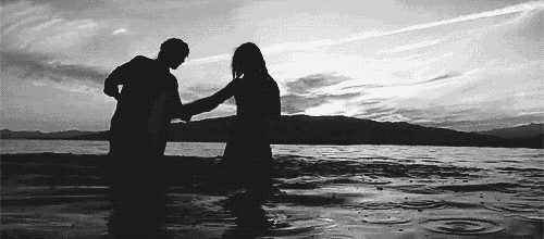 a black and white photo of a man and a woman holding hands in the water