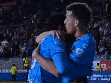 two soccer players are hugging each other in front of a sign that says laboratorio santa maria