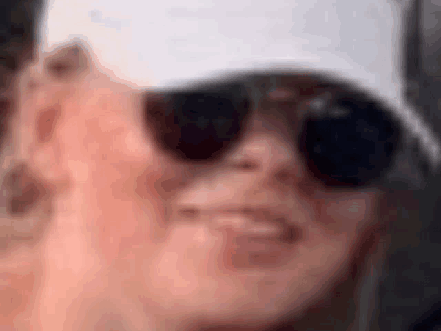 a woman wearing sunglasses and a hat is making a funny face .