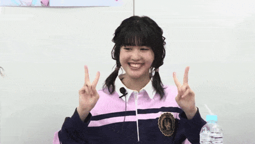 a girl wearing a pink and blue striped shirt is smiling and giving the peace sign