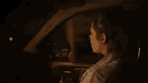 a woman is sitting in the driver 's seat of a car at night looking at her phone .