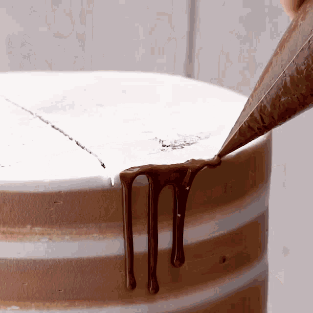 a person is piping chocolate on a cake with a pastry bag