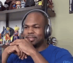 a bald man wearing headphones and a blue shirt is sitting in front of a shelf full of toys .