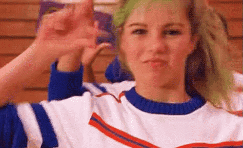 a cheerleader with green hair is making a funny face while giving the middle finger .