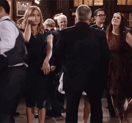 a group of people are dancing in a room with a man in a suit .