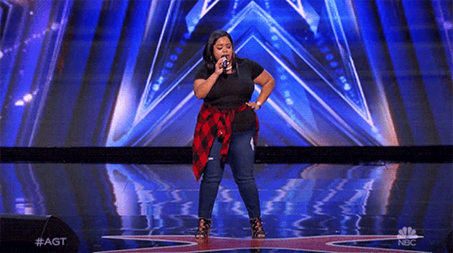 a woman is singing on a stage with a nbc logo behind her