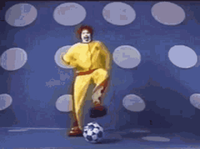 a mcdonald 's character is playing soccer on a blue field .