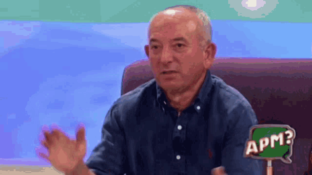 a man is sitting in a chair with his hands out and a sign that says apm .
