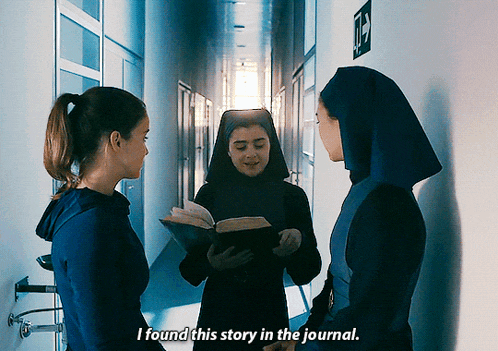 two nuns are standing in a hallway and one is reading a book and the other is saying i found this story in the journal
