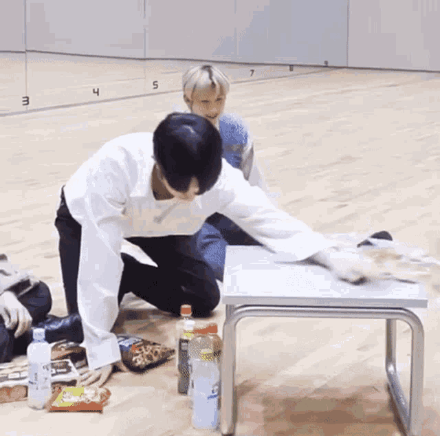 a man is kneeling on the floor next to a table with bottles of water and snacks on it .