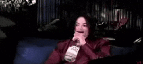a man in a red jacket is sitting on a blue couch with his hand on his chin .