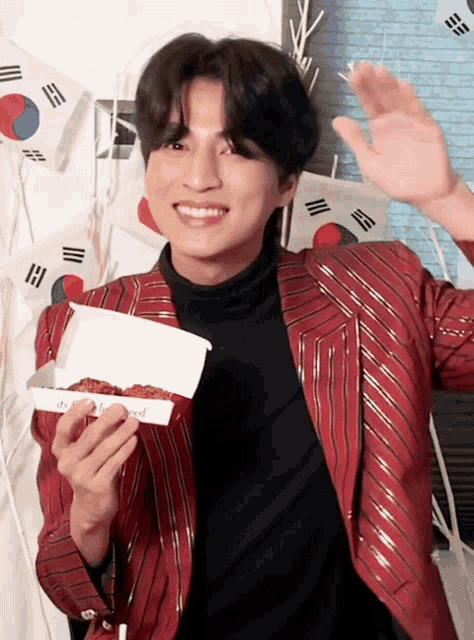 a man in a red jacket is holding a box of food with a korean flag in the background