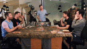 a group of men are sitting around a table with a man holding a clipboard