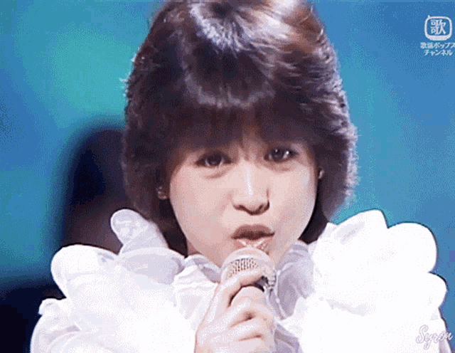 a close up of a woman singing into a microphone with foreign writing on the bottom right corner