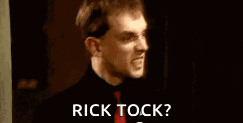 a man with a beard is standing in a dark room and says `` rick tock '' .