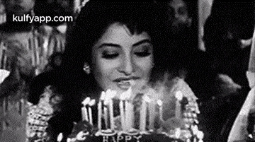 a woman is blowing out candles on a cake in a black and white photo .
