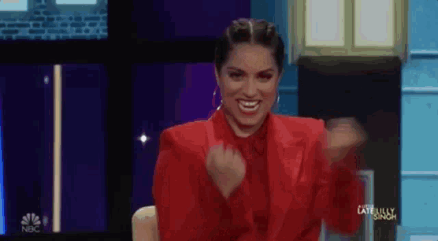 a woman in a red suit is sitting on a stage with her arms in the air and smiling .