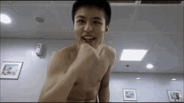 a shirtless young man is standing in a room with his fist in the air .