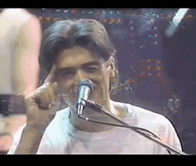 a man singing into a microphone with his finger on his forehead