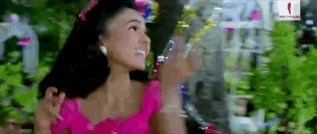 a woman in a pink dress is standing in a forest surrounded by trees and confetti .